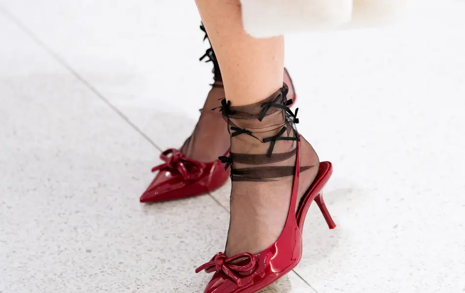 Dame med hvit kåpe, hvit kjole, rød veske, røde pumps, sorte nylonstrømer