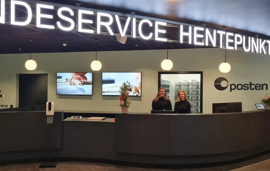 to damer står bak disken til kundeservice, hentepunkt og posten