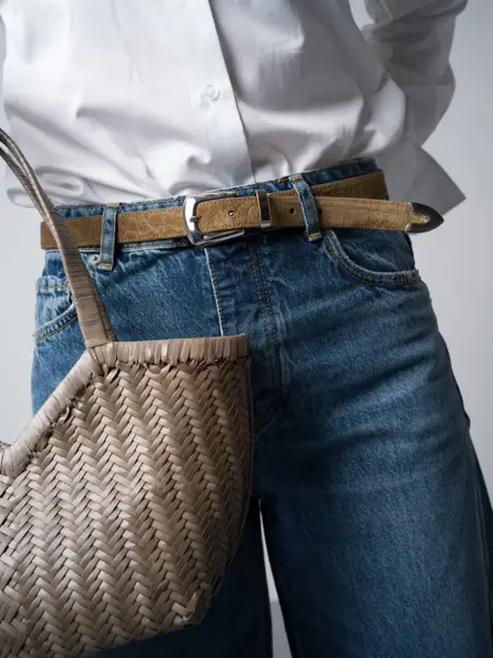 Marianne i hvit skjorte, jeans og smalt beige belte og veske.
