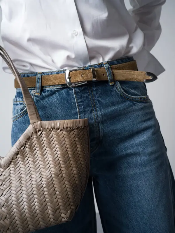 Marianne i hvit skjorte, jeans og smalt beige belte og veske.