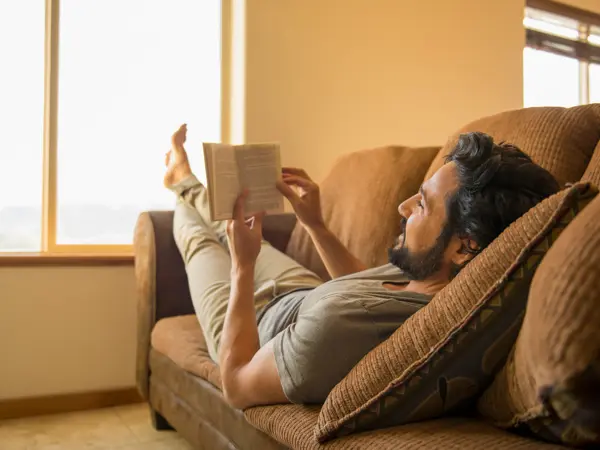 Hispanic man reading book on sofa