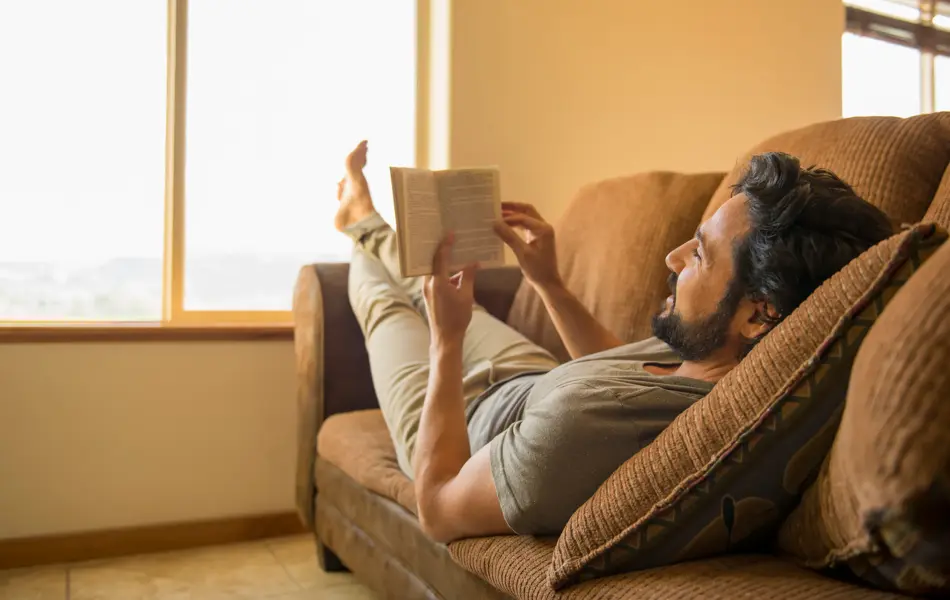 Hispanic man reading book on sofa