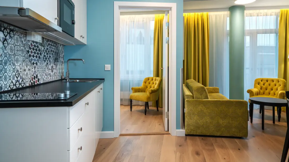 Parkettgulv, blå vegger, kjøkken, gul sofa, gul stol, gule gardiner, Vindu fra gul til tak, stue og soverom. 
