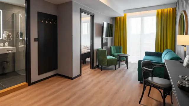 Stue i junior suite med grønne møbler, gule gardiner og parkettgulv.