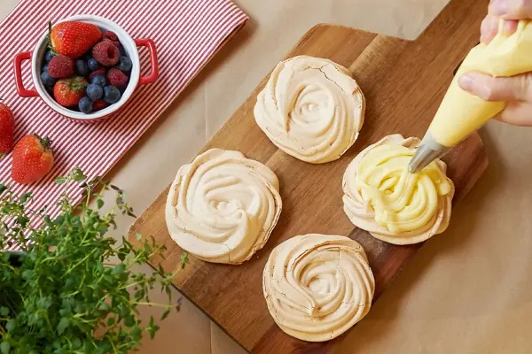 Noen som sprøyter vaniljekrem på marengs