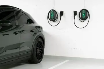 Bakdelen av en mørk bil står parkert i en garasje med to ladekabler på en hvit vegg.