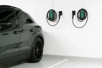 Bakdelen av en mørk bil står parkert i en garasje med to ladekabler på en hvit vegg.