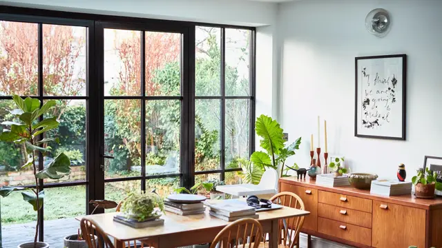 Interiørbilde fra stue som er innredet med 60-tallsinspirerte møbler, store vinduer med sort smijern rundt.