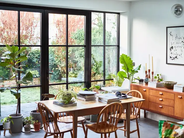 Interiørbilde fra stue som er innredet med 60-tallsinspirerte møbler, store vinduer med sort smijern rundt.