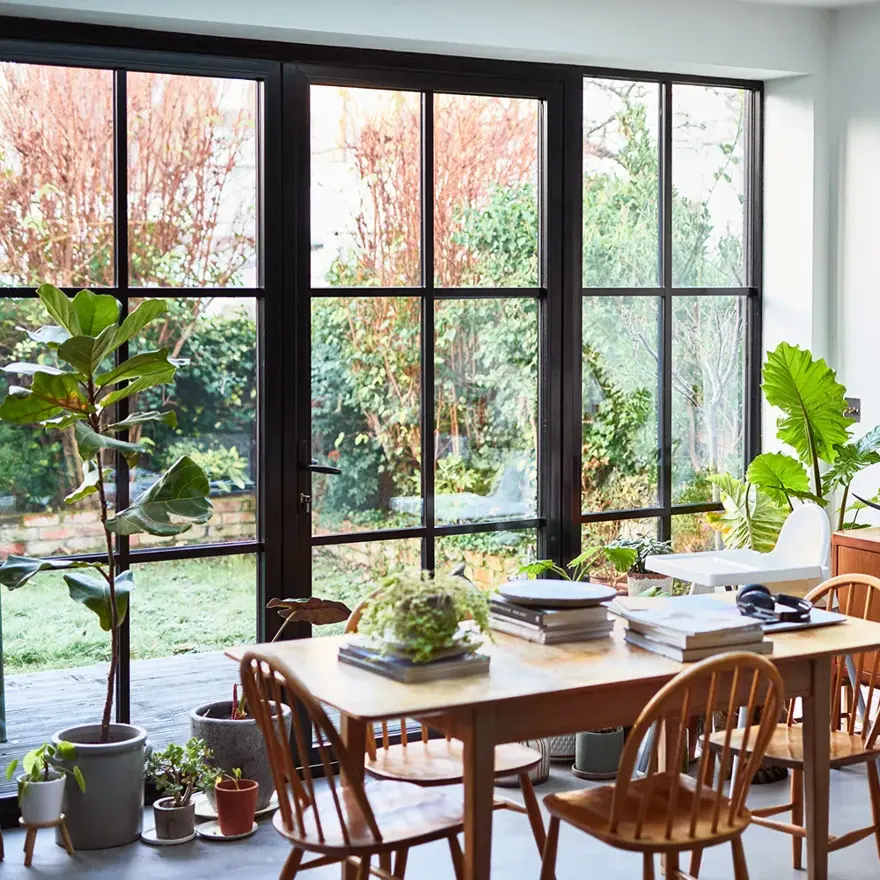 Interiørbilde fra stue som er innredet med 60-tallsinspirerte møbler, store vinduer med sort smijern rundt.