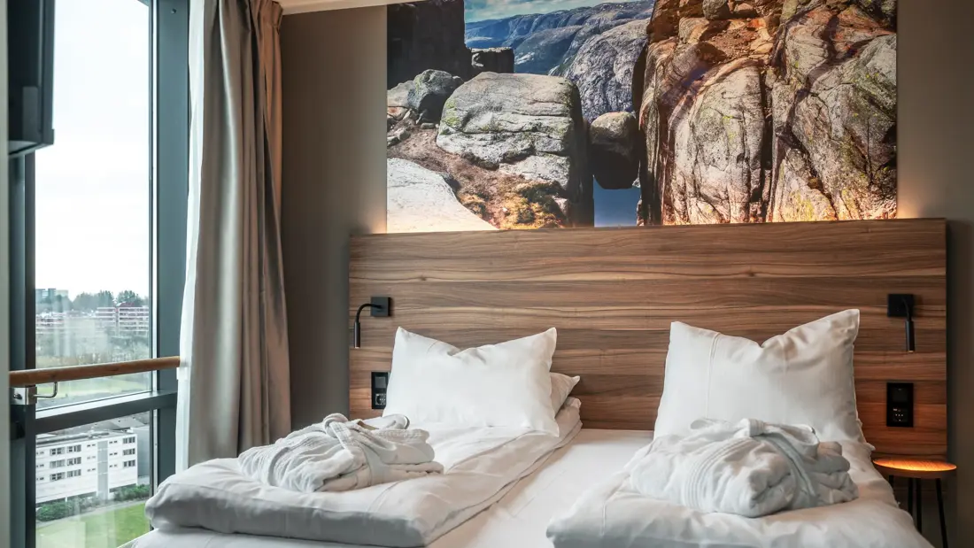 Dobbeltseng med morgenkåper, ved vindu, sengegavl i tre, stort bilde av Kjerag.