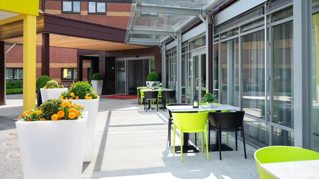 Uteservering på Thon Hotel Bergen Airport med grønne planter og fargerike stoler