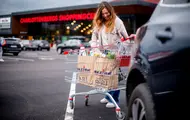 Bildet er tatt utendørs ved kjøpesenteret Charlottenbergs Shoppingcenter og viser en dame i grønn strikkejakke med en handlekurv full av ulike bæreposer.
