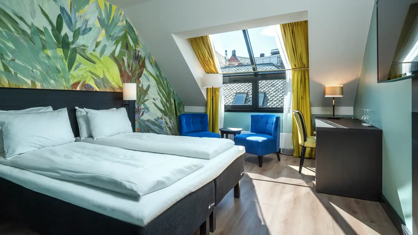 Fargetapetvegg, blå lenestoler, vindu, salongbord, dobbeltseng, TV, skrivebord