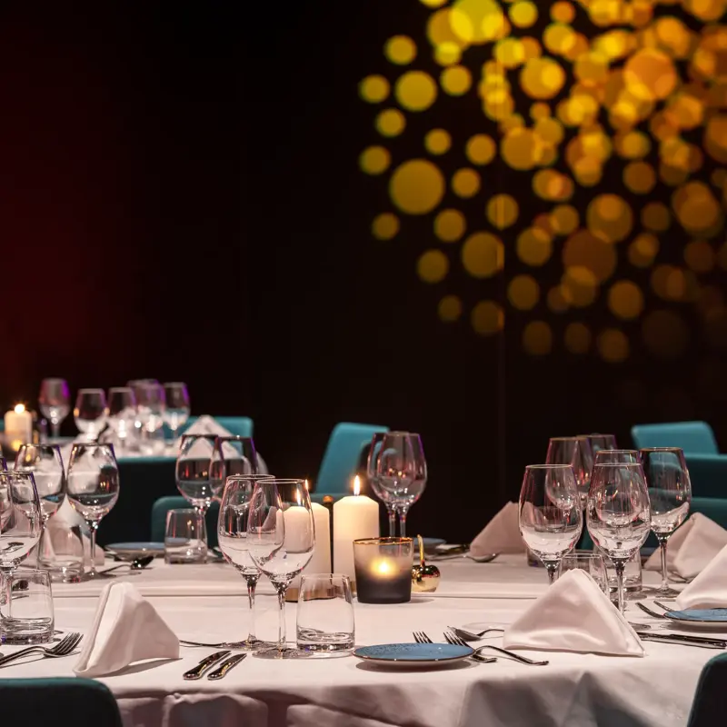 Kveldsstemning, bankett, runde bord med hvite duker og stearinlys. Turkise stoler.