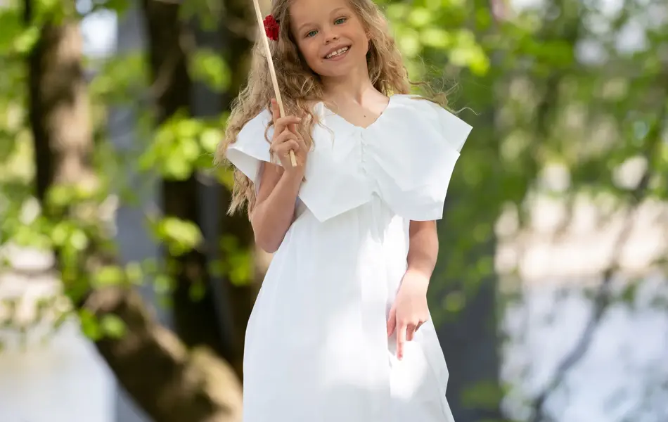 Jente står ute i hvit kjole og hvite sneakers, holder et flagg.