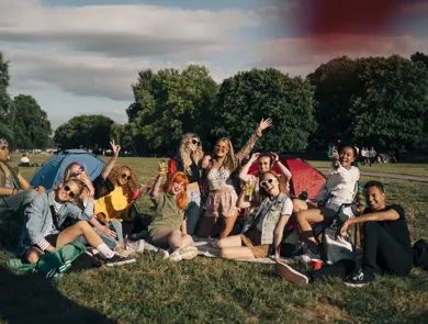 Stor vennegjeng sitter i en grønn park og vinker smilende til kamera