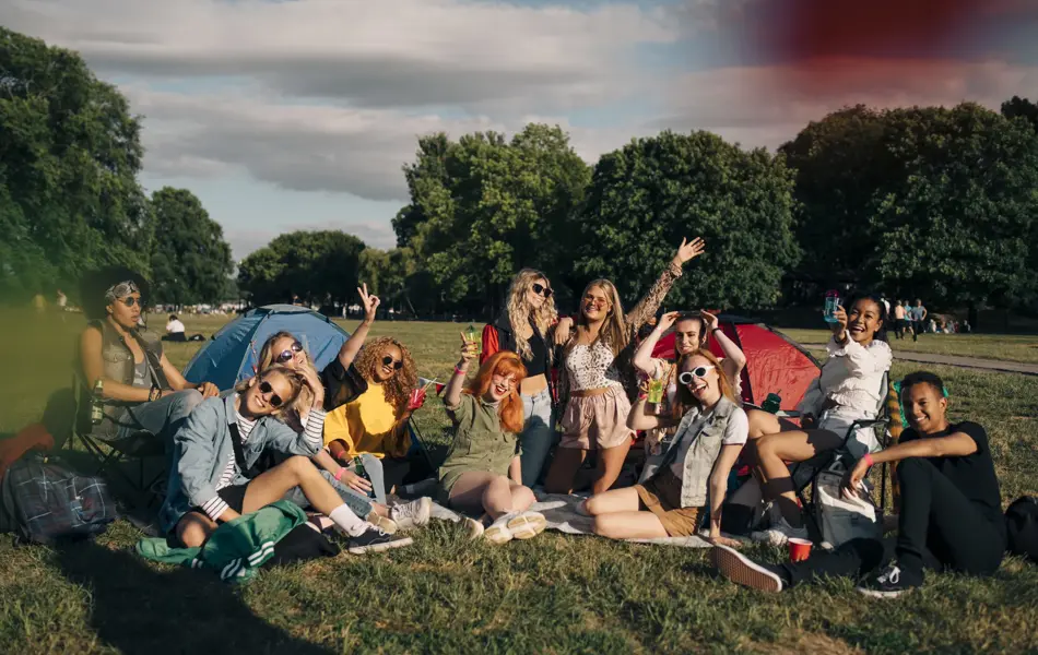 Stor vennegjeng sitter i en grønn park og vinker smilende til kamera