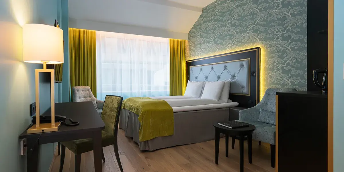 Handikaprom hos Thon Hotel Opera med dobbeltseng, to stoler, skrivebord med tilhørende stol, stort vindu, mønstrete tapet i hvitt og blågrått. Parkettgulv.