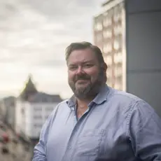 Portrettfotografi av Joachim Langebrekke. Han har på seg en blå skjorte og smiler. 