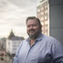 Portrettfotografi av Joachim Langebrekke. Han har på seg en blå skjorte og smiler. 