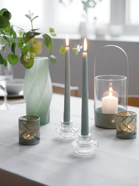 Nærbilde av et bord med stearinlys, telyholdere, lykter og en grønn vase.