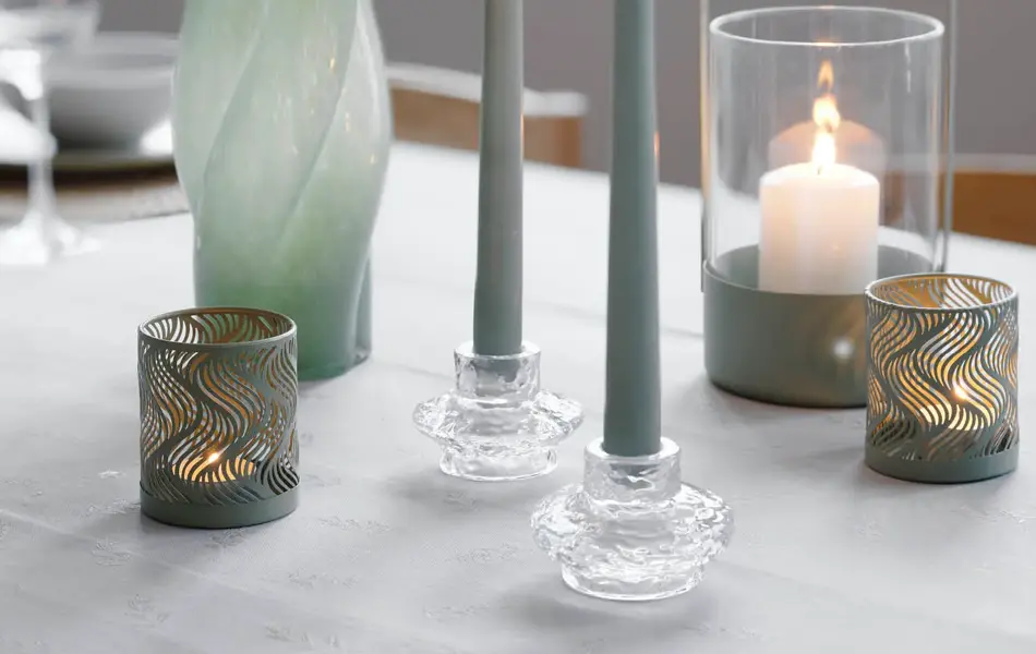 Nærbilde av et bord med stearinlys, telyholdere, lykter og en grønn vase.