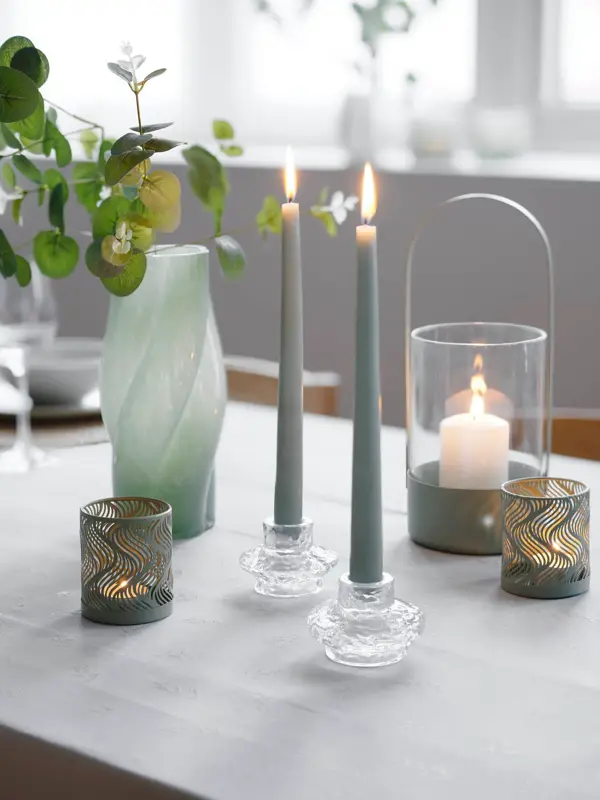 Nærbilde av et bord med stearinlys, telyholdere, lykter og en grønn vase.