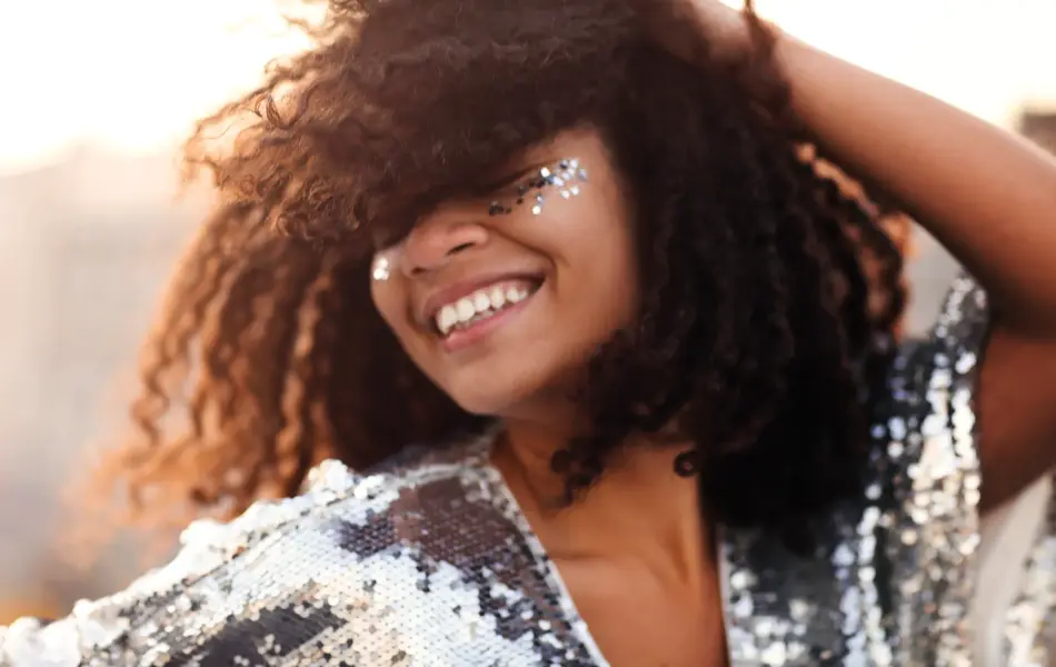 Portrait of overjoyed glamour african american woman with glitter on face in silver sequin dress enjoying outdoor party or event, mixed-race female in festive wear with eyes closed feeling happy