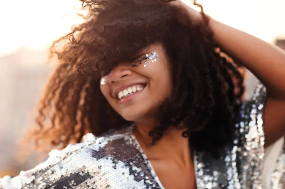 Portrait of overjoyed glamour african american woman with glitter on face in silver sequin dress enjoying outdoor party or event, mixed-race female in festive wear with eyes closed feeling happy