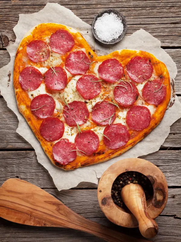 Heart shaped pizza with pepperoni and mozzarella. Valentines day greeting card. Top view