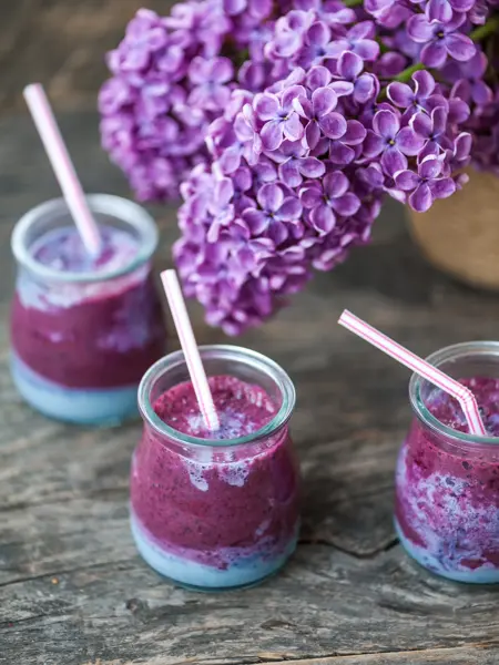 Blueberry smoothie in small jars on a wooden rustic table and lilac flower 