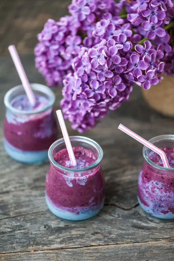 Blueberry smoothie in small jars on a wooden rustic table and lilac flower 