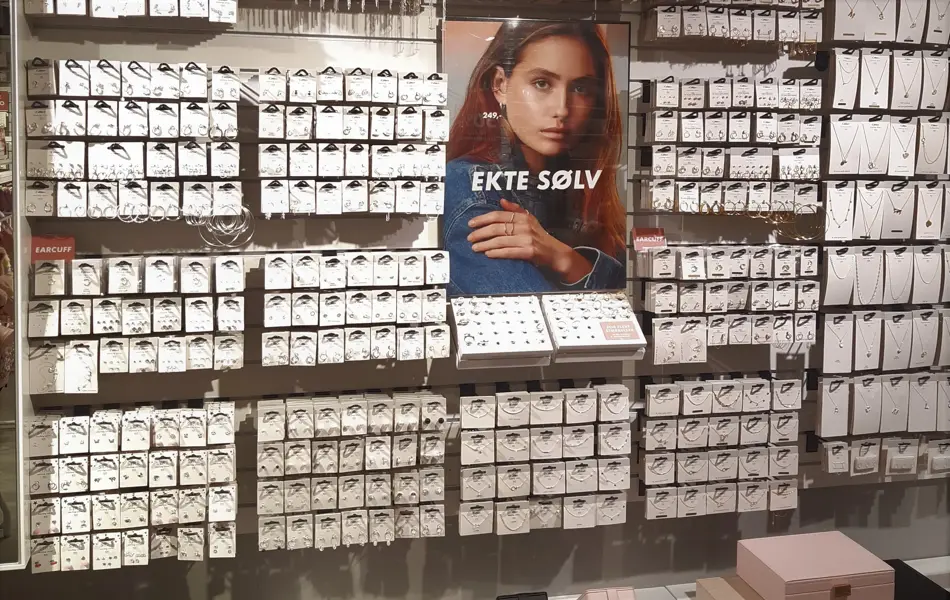 Vegg med en mengde sølvsmykker og bilde av en dame med blå skjorte