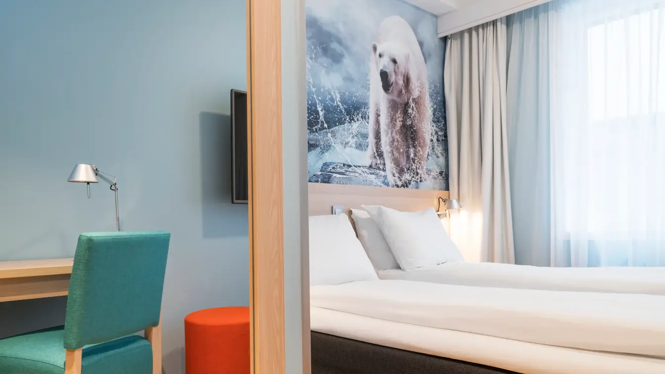 Sengen, kontorplass og tv på et dobbeltrom på Thon Hotel Polar, med et stort bilde av en isbjørn på veggen