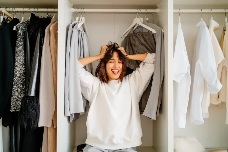 Playful funny dark bobbed haired woman posing in the wardrobe among clothes racks. What to wear, help me
