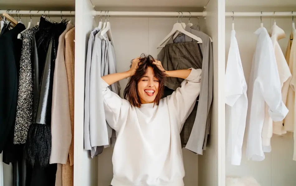 Playful funny dark bobbed haired woman posing in the wardrobe among clothes racks. What to wear, help me