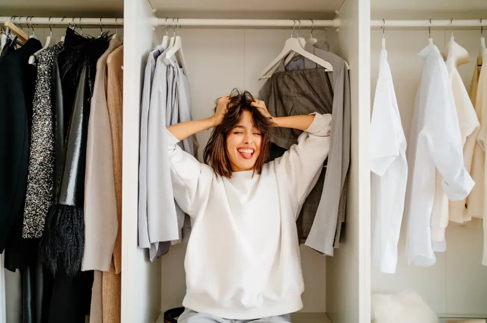 Playful funny dark bobbed haired woman posing in the wardrobe among clothes racks. What to wear, help me