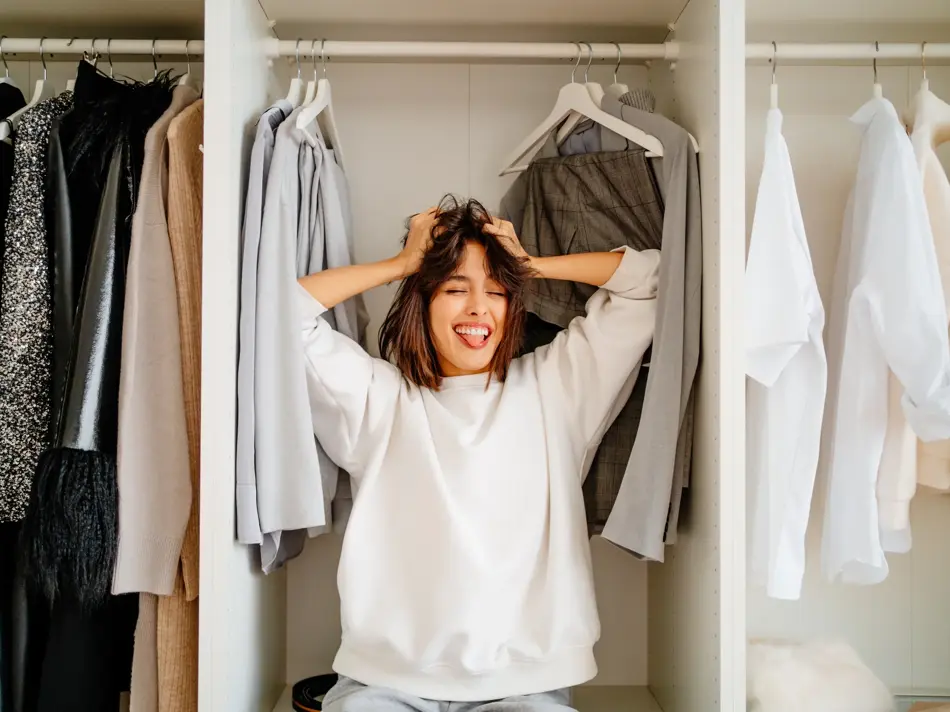 Playful funny dark bobbed haired woman posing in the wardrobe among clothes racks. What to wear, help me