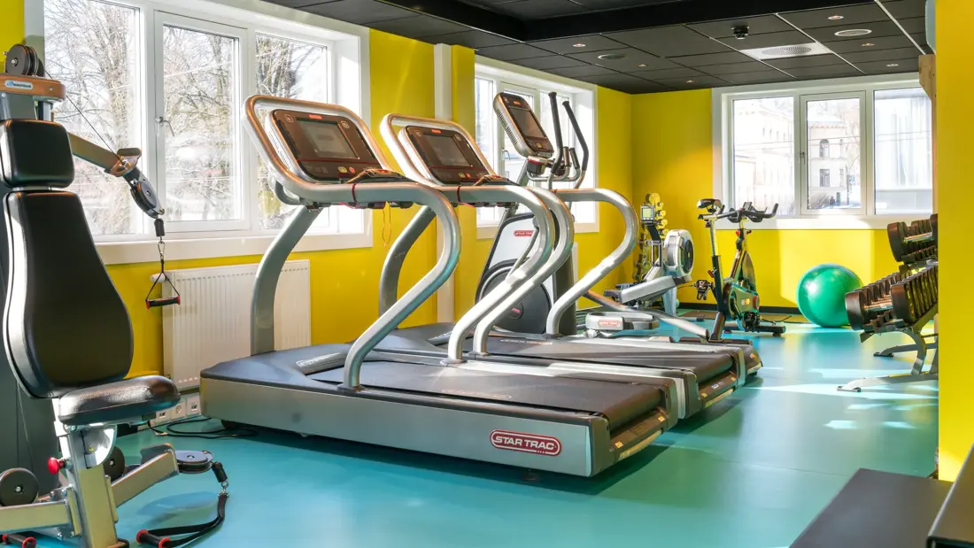 Treningsrom med forskjellige treningsapparater med gule vegger og turkis gulv på Thon Hotel Europa i Oslo sentrum rett ved Slottsparken