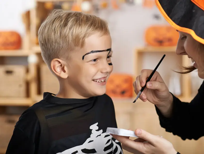 Gutt blir sminket til halloween av dame