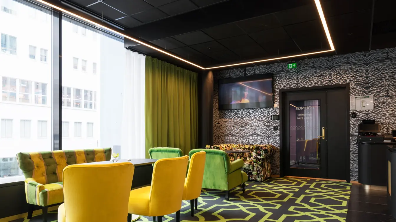 Lounge med mønstret gulvteppe i svart og grønt, gullfargede stoler, lenestoler i forskjellige farger og store vinduer på Thon Hotel Stavanger midt i Stavanger sentrum