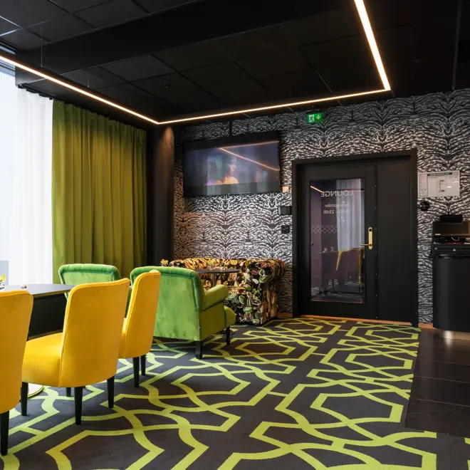Lounge med mønstret gulvteppe i svart og grønt, gullfargede stoler, lenestoler i forskjellige farger og store vinduer på Thon Hotel Stavanger midt i Stavanger sentrum