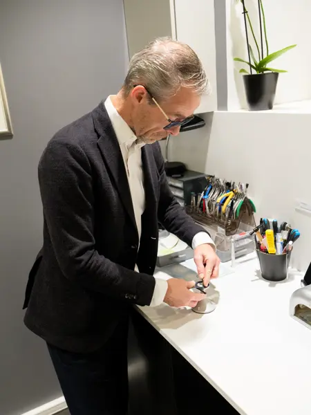 Geir Krogh står ved en benk og reparerer en brille