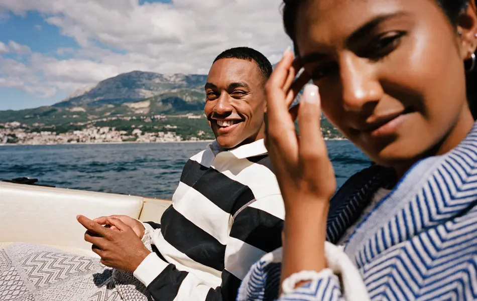 Mann med stripete genser smiler sittende bak hente i båt