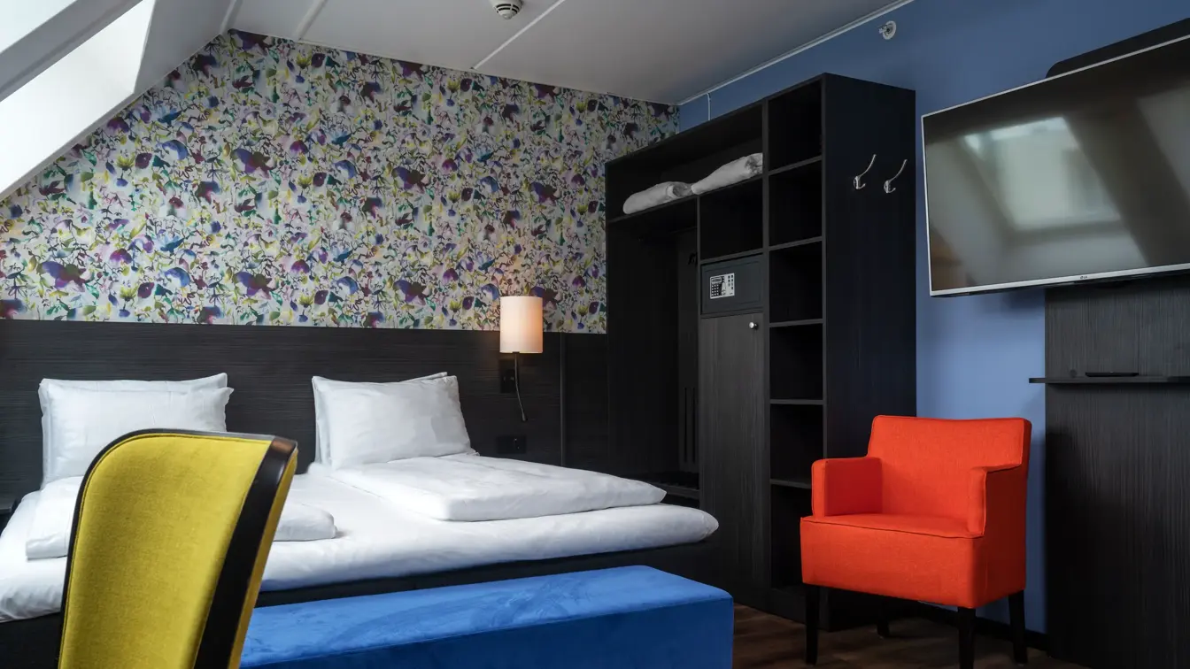 Blomstertapet, dobbeltseng, oransje stol, gul stol, parkettgulv, vindu