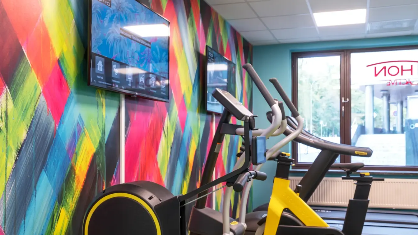 Tapetvegg i forskjellige farger, vindu, gult gulv, diverse apparater. 