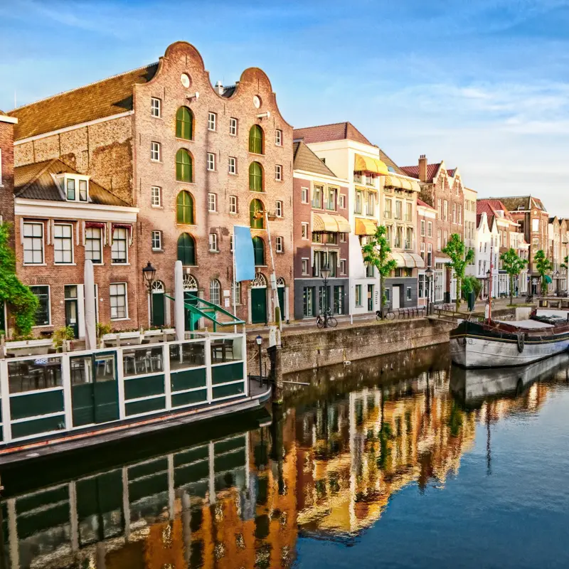 Historic cityscape along a channel in Delfshaven, a district of Rotterdam, the Netherlands. Visible are typical dutch architecture, historic sailing boats, restaurants, colorful reflection in the river, windmills, blue and dramatic cloudscape and beautiful sunset atmosphere.