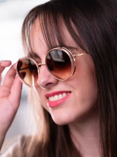 Jente med brunt halvlangt hår og rød leppestift har på seg runde beige solbriller fra Dita
