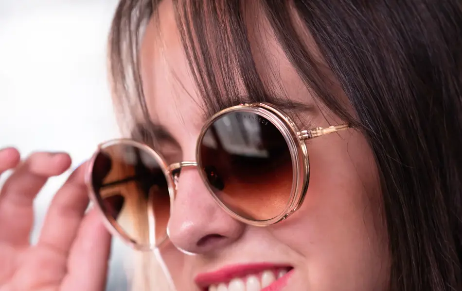 Jente med brunt halvlangt hår og rød leppestift har på seg runde beige solbriller fra Dita